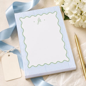 May include: A rectangular notepad featuring a light blue and white vertical striped border with a central white area enclosed by a sage green wavy line. The letters jh are printed in sage green at the top center of the white space.