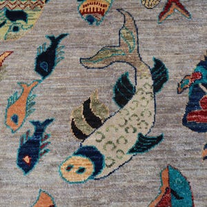 May include: A woven rug featuring a light brown background with a repeating pattern of stylised fish in various colours including dark blue, orange, red, and teal. The central fish is large and cream-coloured with dark blue and green accents.