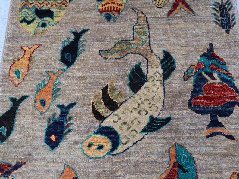 May include: A woven rug featuring a light brown background with a repeating pattern of stylised fish in various colours including dark blue, orange, red, and teal. The central fish is large and cream-coloured with dark blue and green accents.