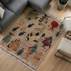May include: A rectangular area rug featuring a tan background with a variety of colourful fish illustrations in shades of red, blue, yellow, and green. The rug has a textured surface and is finished with decorative fringe along the shorter edges.