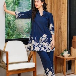 Könnte beinhalten: Ein marineblaues zweiteiliges Outfit mit Tunika und Hose. Die Tunika hat einen V-Ausschnitt und Blumenstickereien am Saum und an den Ärmeln. Die Hose hat passende Blumenstickereien an den Knöcheln. Das Outfit ist aus einem weichen, fließenden Stoff gefertigt.