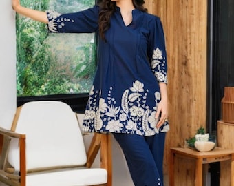 Puede incluir: Un conjunto de dos piezas azul marino con túnica y pantalón. La túnica tiene cuello en V y bordados florales en el dobladillo y las mangas. El pantalón tiene bordados florales a juego en los tobillos. El conjunto está hecho de una tela suave y fluida.