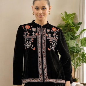 May include: A black velvet jacket with floral embroidery in shades of orange, pink, and white. The jacket has a mandarin collar and a central zip. The detailed embroidery covers the chest and sleeves, creating a bohemian style.