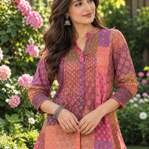 May include: A long-sleeved button-down shirt featuring a patchwork design with various floral and geometric patterns in shades of pink, orange, purple, and brown. The shirt has a mandarin collar, three-quarter length sleeves with smocked cuffs.