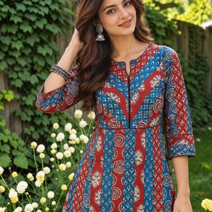 May include: A three-quarter sleeve tunic featuring a vibrant pattern of alternating vertical stripes in deep red and blue. The fabric displays intricate circular and floral motifs in white and dark blue. It has a notched neckline with black trim.