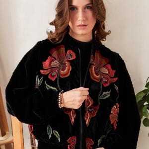 May include: Black velvet bomber jacket with a floral embroidery design in red, orange, and green. The jacket has a zipper closure and a stand-up collar. The sleeves are long and the jacket is slightly oversized.