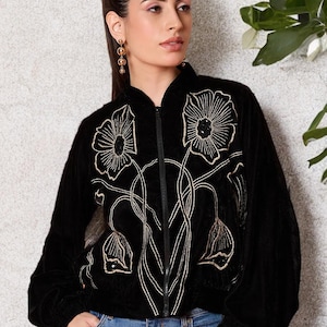 May include: Black velvet bomber jacket with gold floral embroidery. The jacket features a zip-up front, a stand-up collar, and long sleeves. The floral design is embroidered in a gold thread, creating a striking contrast against the black fabric.