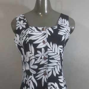 May include: A black and white floral print dress with a square neckline and button-down front. The dress features a tropical leaf and flower pattern. The dress is sleeveless and has a knee-length hemline.