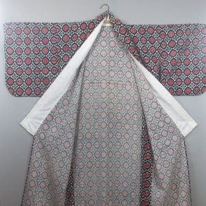 May include: A patterned kimono with a black background and red and white circular designs. The interior lining features a similar pattern in pink and gray. The kimono is open, revealing the interior design and white collar.
