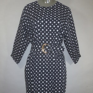 May include: A black and white polka dot dress with a gold belt. The dress has a round neckline and three-quarter sleeves.