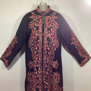 May include: Black long coat with intricate floral embroidery in shades of coral and peach. The coat features a mandarin collar, long sleeves, and a central closure. The embroidery is detailed, covering the front, sleeves, and collar.