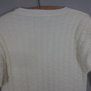 May include: A white quilted sweater with a crew neck.
