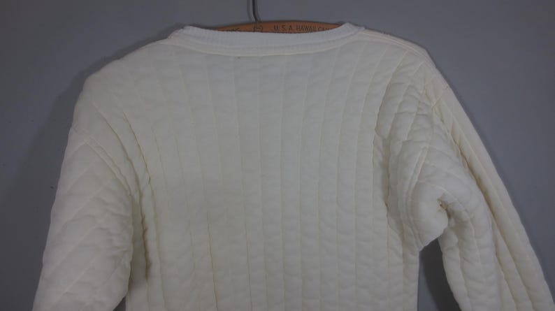 May include: A white quilted sweater with a crew neck.