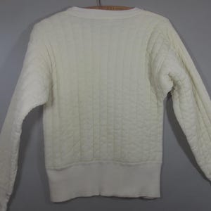 May include: A white quilted sweater with a crew neck and long sleeves.