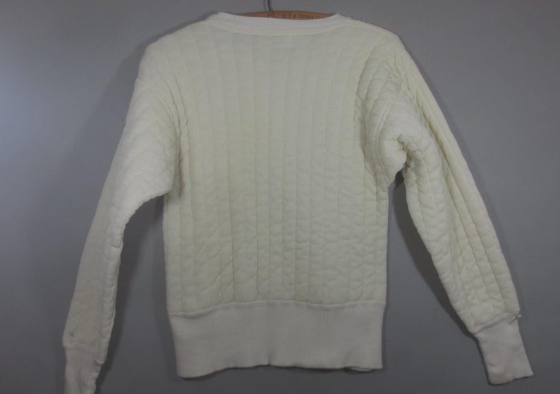 May include: A white quilted sweater with a crew neck and long sleeves.