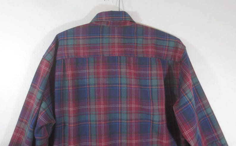 May include: A long-sleeved plaid shirt in shades of red, blue, green, and white. The shirt has a button-down collar and a button-up front.