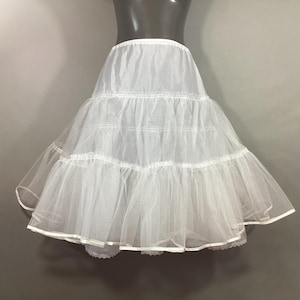 May include: A white petticoat with multiple layers of tulle, creating a full, flared silhouette. The petticoat is designed to add volume under a skirt or dress. The hemline is finished with a white trim.