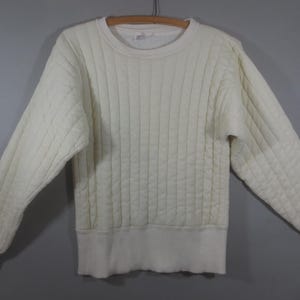 May include: A white quilted sweater with a crew neck and long sleeves.