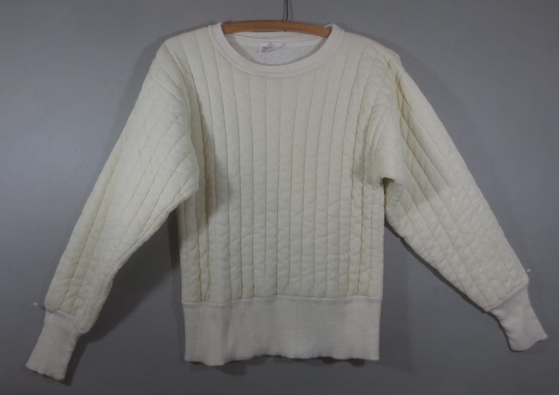May include: A white quilted sweater with a crew neck and long sleeves.