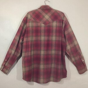 Puede incluir: Camisa de manga larga con un estampado a cuadros en rojo, beige y marr&oacute;n. La camisa est&aacute; abotonada y colgada de una percha met&aacute;lica. La parte trasera de la camisa es visible, mostrando la pieza del canes&uacute; y los pu&ntilde;os abotonados.