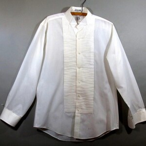 May include: A white long-sleeve dress shirt with a pleated front and a classic collar. The shirt has a button-up closure and is made of a smooth, lightweight fabric.