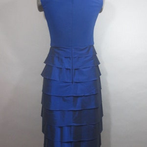 K&ouml;nnte beinhalten: Ein &auml;rmelloses Kleid in K&ouml;nigsblau mit einem Stufenrock. Das Kleid hat ein figurbetontes Oberteil und einen flie&szlig;enden Rock.