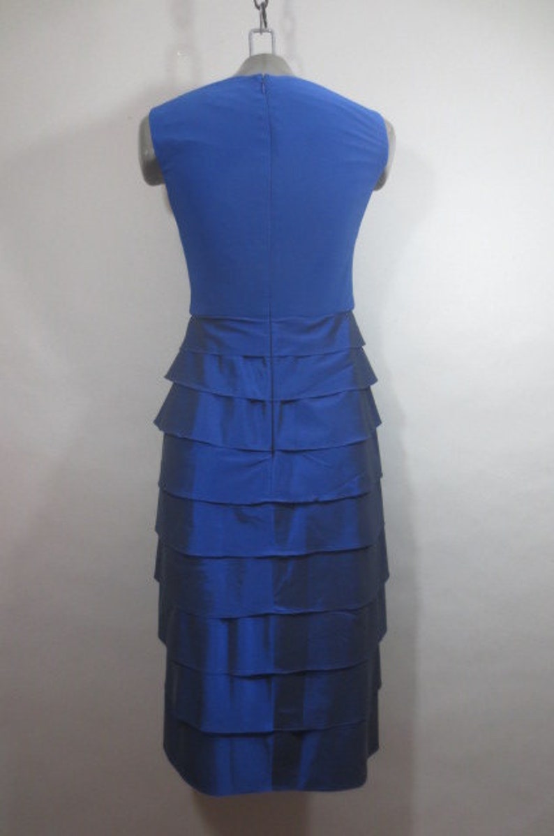 K&ouml;nnte beinhalten: Ein &auml;rmelloses Kleid in K&ouml;nigsblau mit einem Stufenrock. Das Kleid hat ein figurbetontes Oberteil und einen flie&szlig;enden Rock.