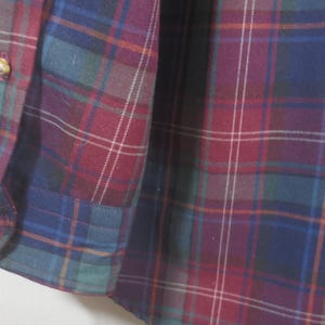 May include: Close-up of a red, blue, and green plaid fabric. The fabric has a subtle sheen and a soft texture.