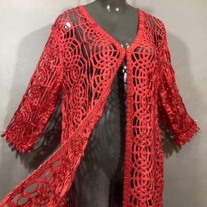 May include: A red crochet cardigan with a long, open front and a delicate, lacy pattern. The cardigan has a relaxed fit and three-quarter sleeves.