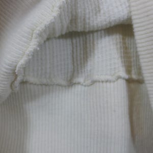 May include: Close-up of the inside of a white ribbed sweater. The fabric is soft and stretchy.