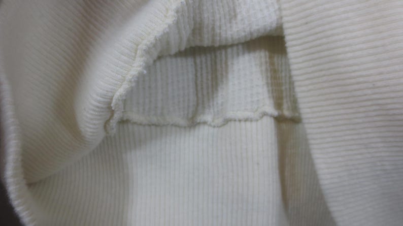May include: Close-up of the inside of a white ribbed sweater. The fabric is soft and stretchy.