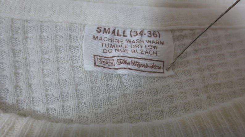 May include: A white tag with brown text that reads "SMALL (34-36)" and "MACHINE WASH WARM TUMBLE DRY LOW DO NOT BLEACH" with the Sears logo and "The Men's Store" below the text.