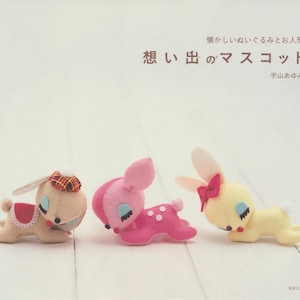 May include: A book cover featuring three plush animal toys: a tan bunny with a plaid hat, a pink deer with white spots, and a yellow bunny with a red bow. The Japanese text reads "Memories Mascot."