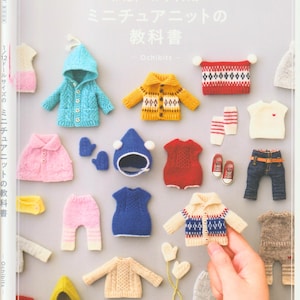 May include: A selection of miniature knitted doll clothes, including jackets, hats, trousers, and dresses in various colours. The image also shows tiny shoes and a pair of jeans. The text on the book cover reads "1/12 Doll Size Miniature Knit Textbook."