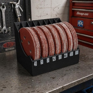 May include: A black plastic organizer rack holding multiple stacks of circular red sandpaper discs. The front of the rack features white printed numbers 40, 60, 80, 120, 180, 220, 400, and 600, indicating the grit levels for each organized section.