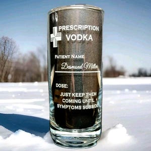 May include: A clear glass tumbler featuring a black label with white text that reads Prescription Vodka, Patient Name Desmond Miller, and Dose: Just keep them coming until symptoms subside, accompanied by a white medical cross icon.
