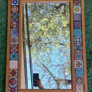 May include: A rectangular wall mirror featuring a wooden frame bordered by a mosaic of colorful square ceramic tiles. Each tile displays a unique, intricate pattern in various shades of blue, red, yellow, and white, creating a vibrant decorative border.