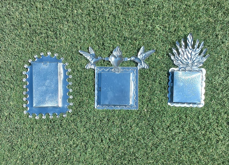 Peut inclure: Trois cadres m&eacute;talliques argent&eacute;s avec des motifs d&eacute;coratifs. L'un a un bord festonn&eacute;, un autre repr&eacute;sente des colibris et un c&oelig;ur, et le troisi&egrave;me a un sommet en forme de flamme. Tous ont un espace rectangulaire pour une photo.