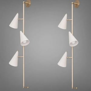 Puede incluir: Dos apliques de pared con un diseño minimalista. Cada aplique presenta una estructura metálica dorada con tres pantallas blancas en forma de cono. Los apliques están montados sobre un fondo gris.