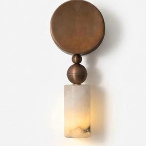 Può includere: Applique da parete con una piastra posteriore circolare in bronzo e un paralume cilindrico in alabastro bianco sporco. Il paralume è illuminato dall'interno, creando un bagliore caldo. L'applique ha un dettaglio decorativo a sfera e palla in bronzo.