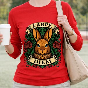 May include: Red long-sleeve shirt featuring a detailed illustration of a rabbit with blue eyes, surrounded by roses and foliage. The design includes the words "CARPE" and "DIEM" on banners. The shirt is a solid red color.