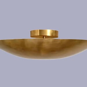 Può includere: Una ciotola poco profonda color oro con un centro circolare rialzato. La ciotola ha una forma ampia e curva e una superficie liscia e riflettente. Il design è semplice ed elegante, adatto a scopi decorativi.