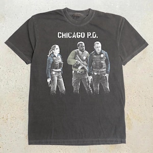 May include: A charcoal grey short-sleeve t-shirt featuring a white graphic print of three police officers in tactical gear. Above the figures, the text CHICAGO P.D. is printed in a distressed white font. The shirt has a crew neckline and a relaxed fit.