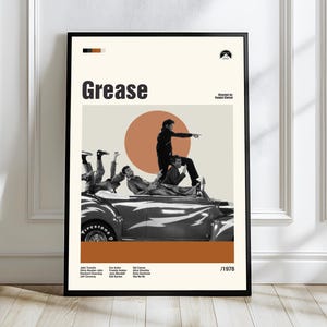 Può includere: Un poster incorniciato del film "Grease", con un design retrò. Il poster presenta il titolo in nero, un'immagine in seppia di attori su un'auto, un cerchio arancione e il logo Paramount.