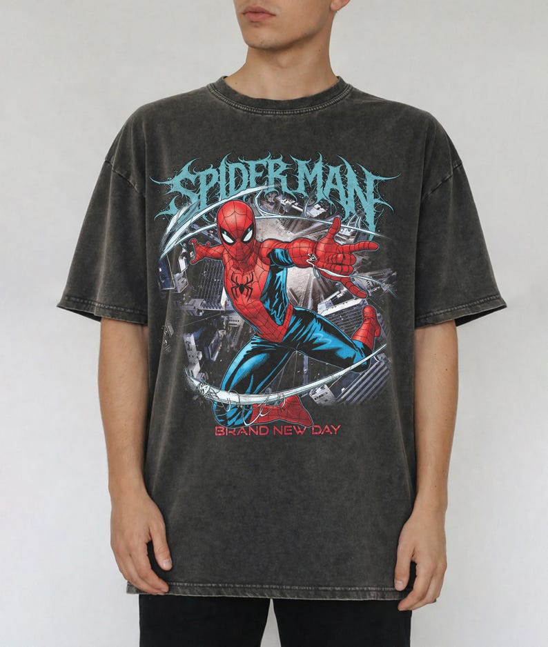May include: A charcoal gray, acid-washed short-sleeve t-shirt featuring a graphic print of Spider-Man in a dynamic pose. The text "SPIDER-MAN" appears in a stylized font above the character, with the words "BRAND NEW DAY" printed in red below.