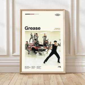 Può includere: Un poster incorniciato con il film "Grease". Il poster ha uno sfondo color crema con una foto del cast che posa attorno a un'auto rossa. Il titolo "Grease" è in alto, con l'anno "/78" in basso.