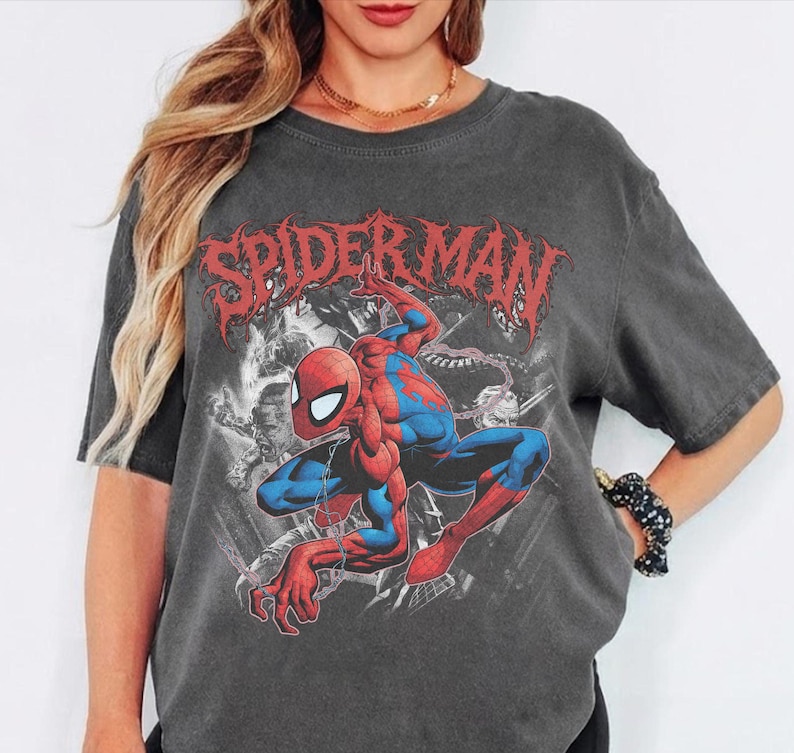 May include: A charcoal gray short-sleeve t-shirt featuring a large graphic print of the Marvel character Spider-Man in a crouching pose. The design includes the red text Spider-Man in a stylized font above the character and black and white imagery.