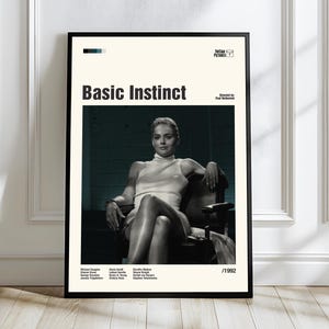 May include: A framed movie poster for "Basic Instinct" featuring a black and white image of a woman in a chair. The poster has the movie title, credits, and the year 1992.