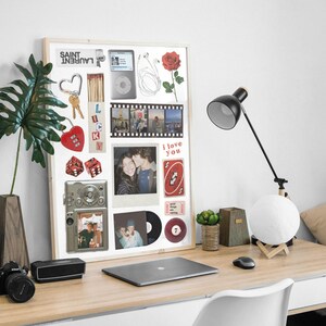 Peut inclure: Un collage encadré en bois avec divers objets, dont une rose rouge, un appareil photo vintage, un lecteur de musique et une bande de film. Le collage comprend également une photo, un jeu de cartes et les mots "i love you". Une lampe de bureau et un ordinateur portable sont également visibles.