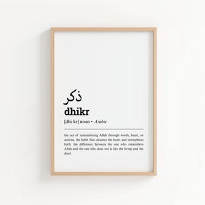 May include: A framed print with the Arabic word "dhikr" in black, along with its English transliteration and definition. The print is in a light wood frame and hangs on a white wall.
